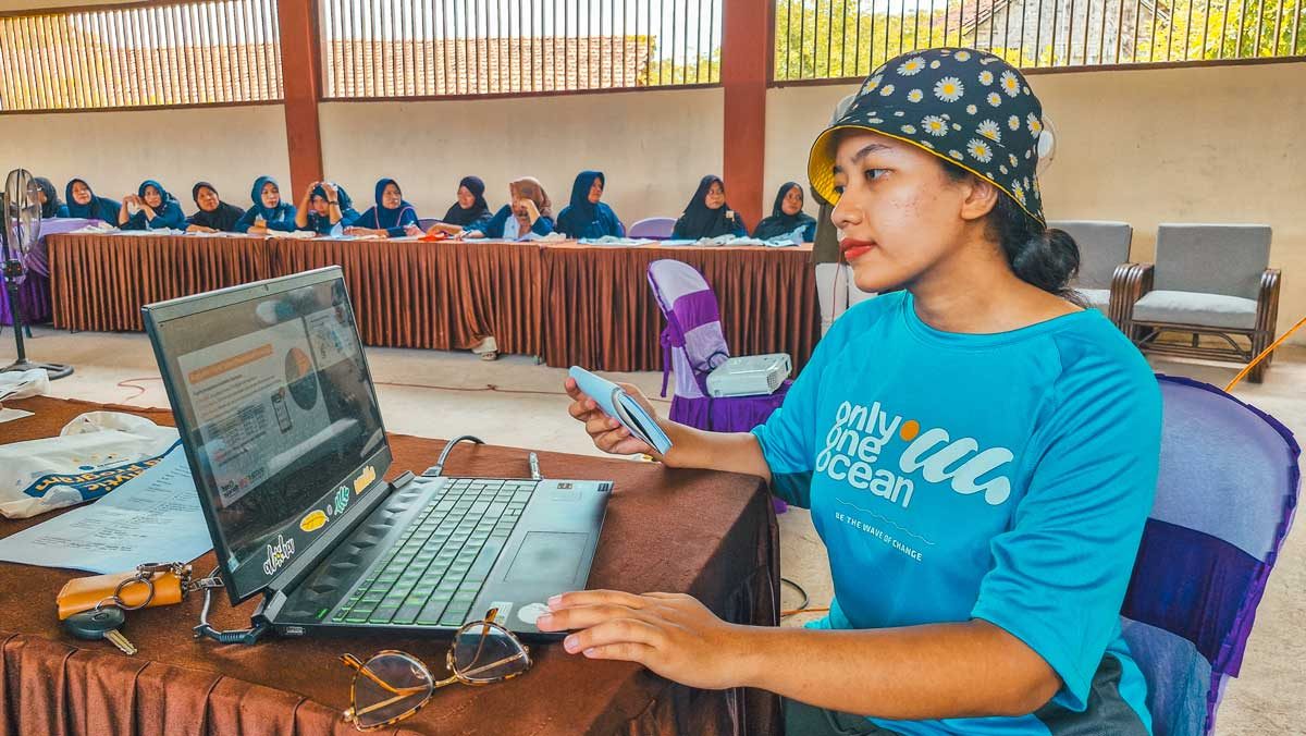 A financial literacy session with women attendees, taught by a young Indonesian woman in an O3 shirt.