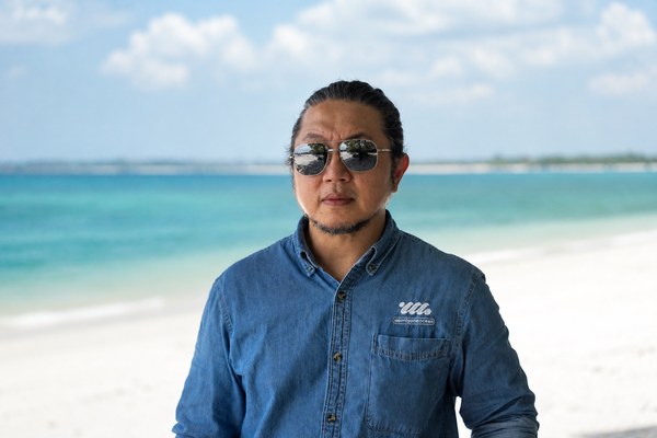 Portrait of Jordan Y. Xu on a Belitung beach in a denim O3 shirt, ocean behind.